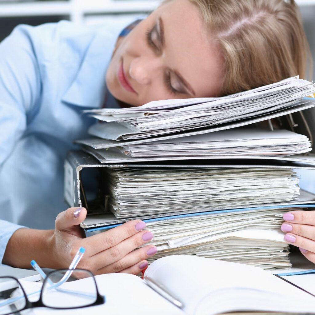 Femme épuisée endormie sur une pile de dossiers, symbole de la surcharge mentale et de la sauveuse qui s’oublie en voulant tout gérer.