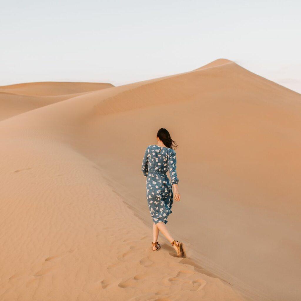Femme marchant seule dans de hautes dunes de sable, symbolisant la mode du développement personnel qui envoie tout le monde dans le désert pour “évoluer”